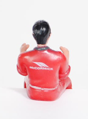 Traktorfahrer mit eisengrau/rotmetallicfarbiger Overal, schwarze Haare, McCormick Logo auf der Brust
